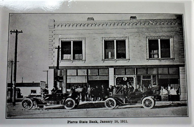 A brick corner building with tall windows and a bank sign above the door.