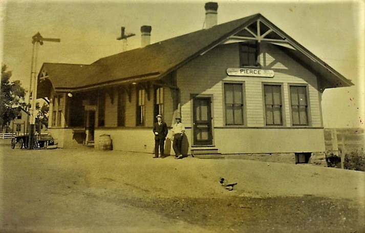 A single-storey wooden railway depot with men standing on the platform.